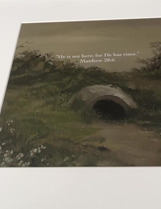 Close view of He Has Risen showing the open and empty tomb cut into a green hillside with the words from Matthew 28:6 set above it