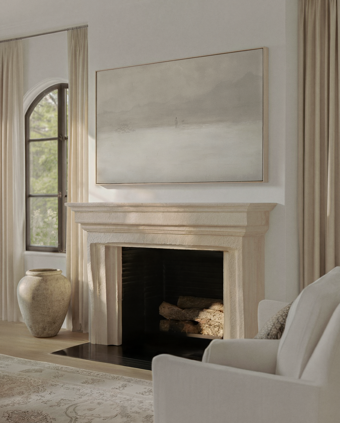 Large neutral Christian canvas hung above a limestone fireplace in a cream living room with an arched window and a white armchair