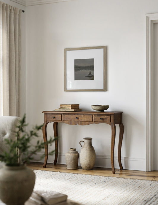 Psalm 46 Be Still matted print in a light wood frame hung above a carved wood console with stone vases and an olive branch